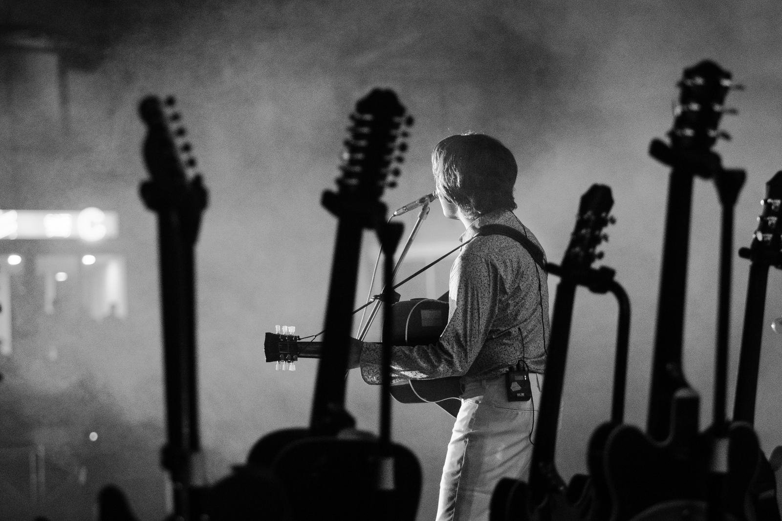 Foto hitam putih gitaris di antara deretan gitar